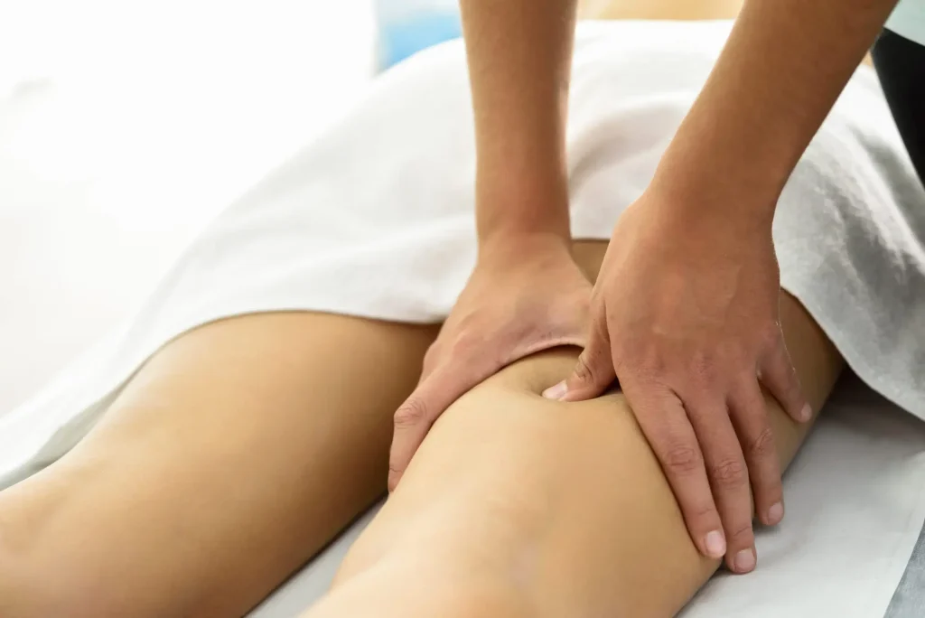 Masseur effectuant un massage thérapeutique sur la cuisse d'une patiente allongée sur une table de massage.